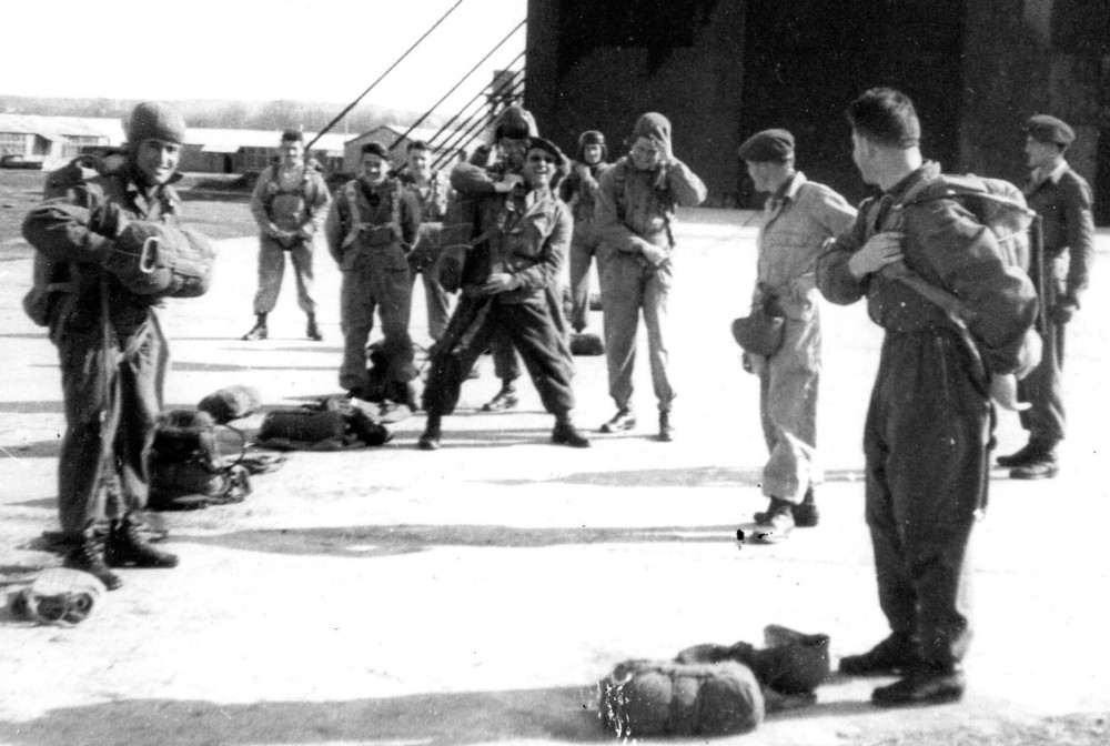 "Des parachutistes s' équipent pour le saut .En arrière plan un hangar identique à ceux que l'on pouvait encore voir au Camp GUYNEMER dans les années 80/90